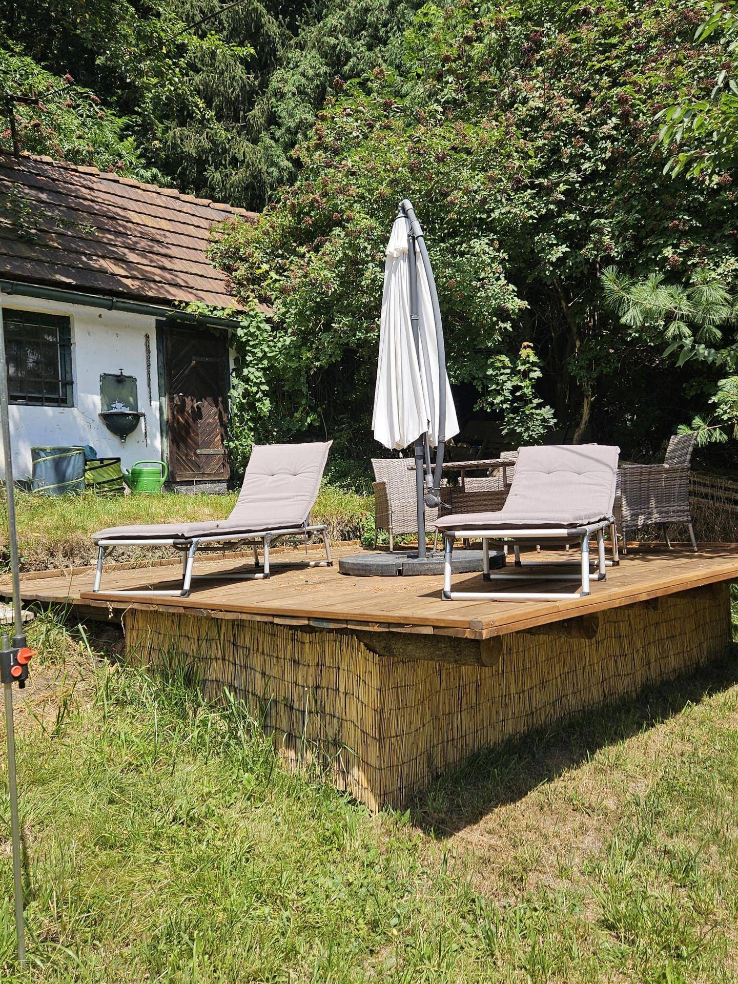 Holzdeck mit Sonnenliegen und Sonnenschirm, ideal zum Entspannen im Gartenbereich.