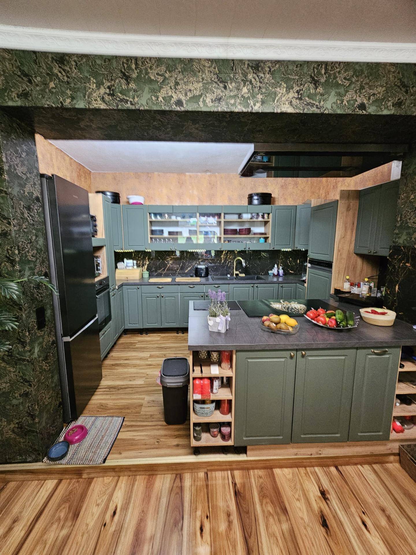 Moderne Küche mit grünen Schränken, Kücheninsel und Holzboden, gut ausgestattet.