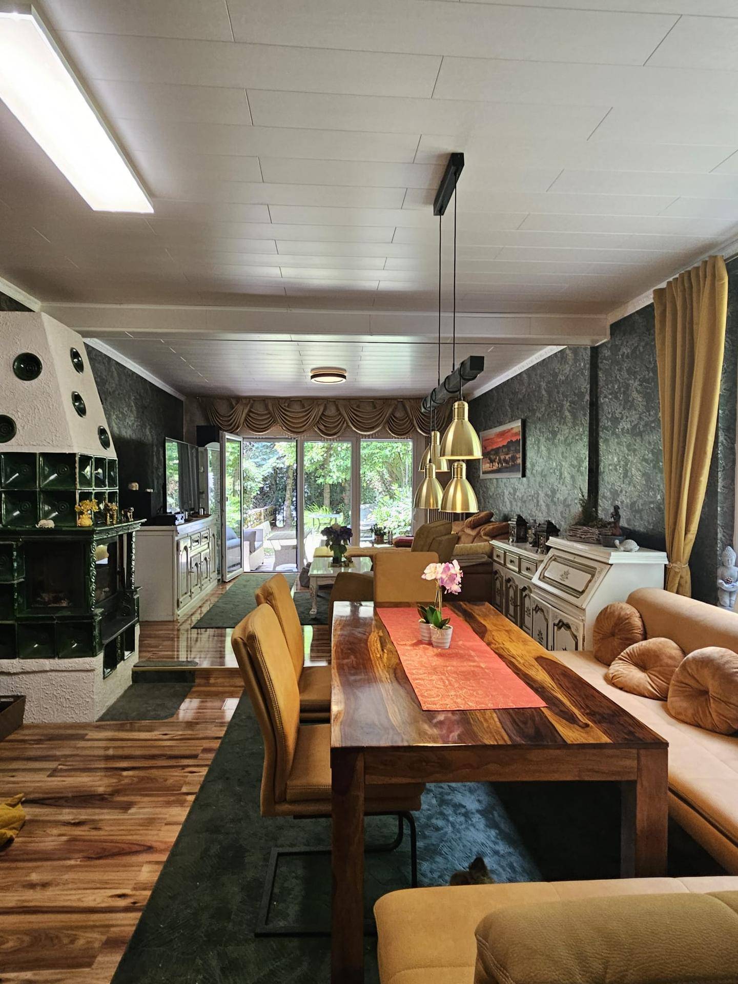 Geräumiger Wohn-Essbereich mit Holzboden, Kachelofen und Zugang zur Terrasse.