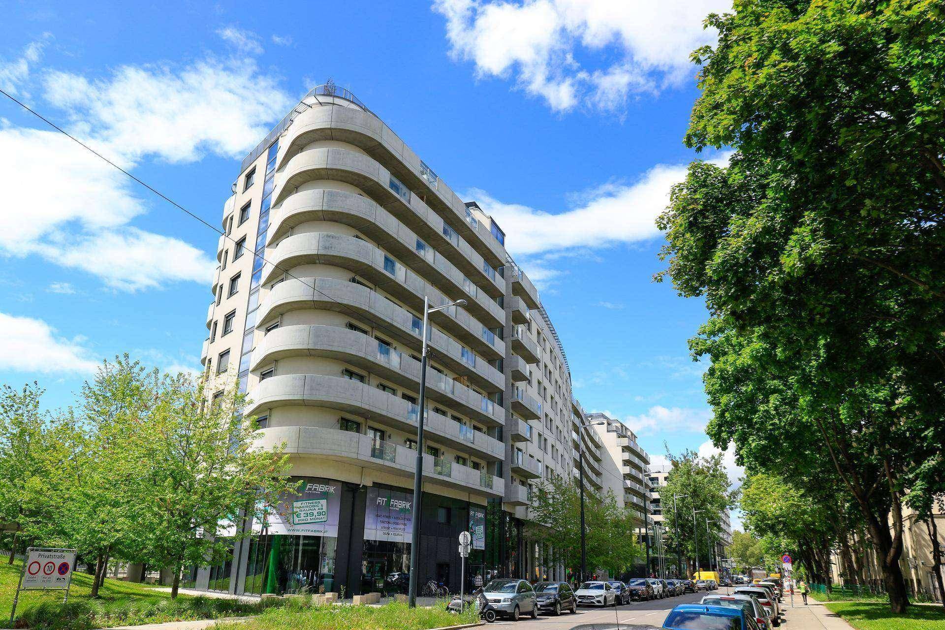 Lange Fassade eines modernen Wohngebäudes mit vielen Balkonen entlang einer Straße.
