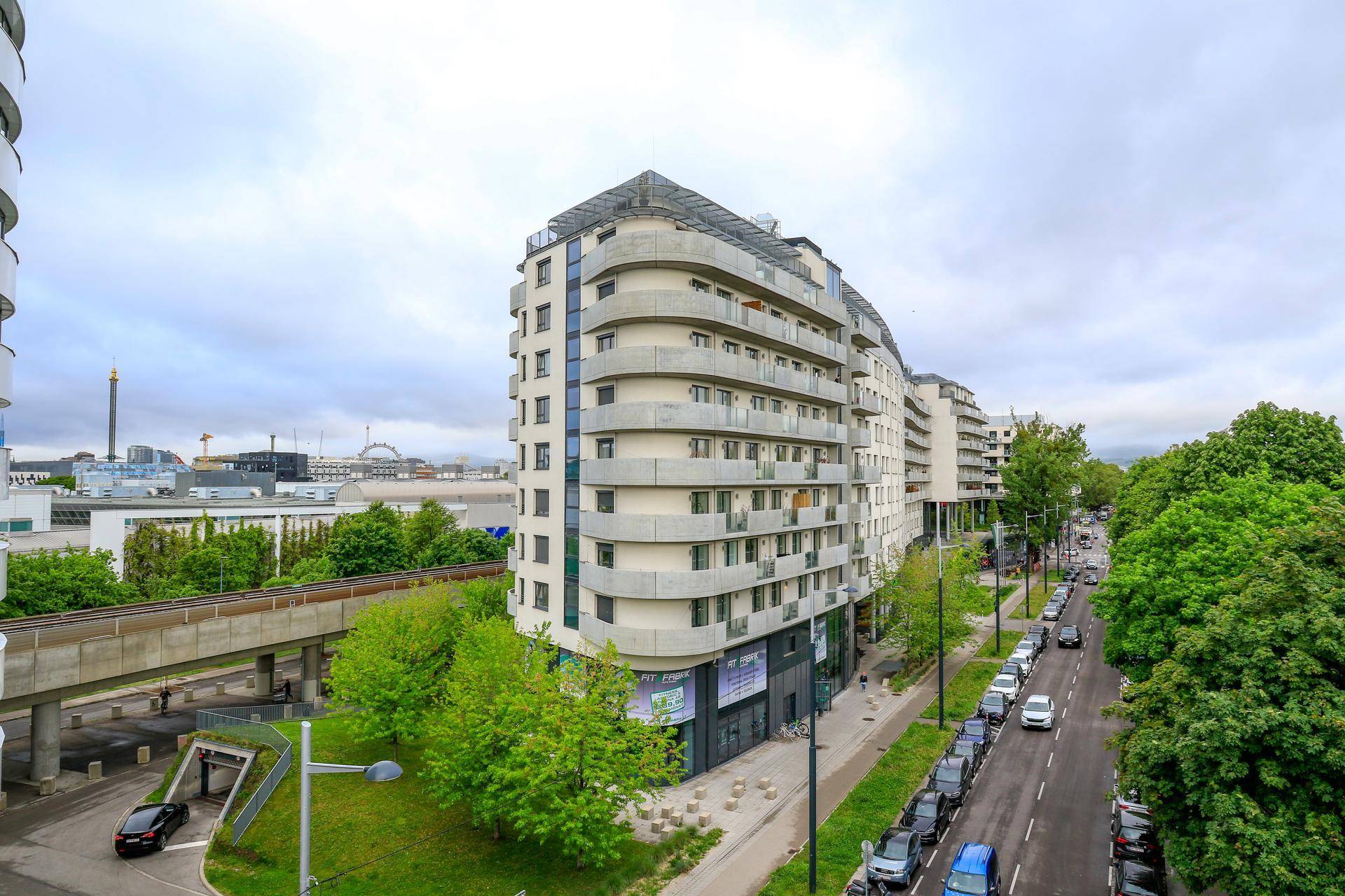 Wohngebäude mit geschwungener Fassade, Balkonen und Blick auf die Stadt und umliegende Infrastruktur.