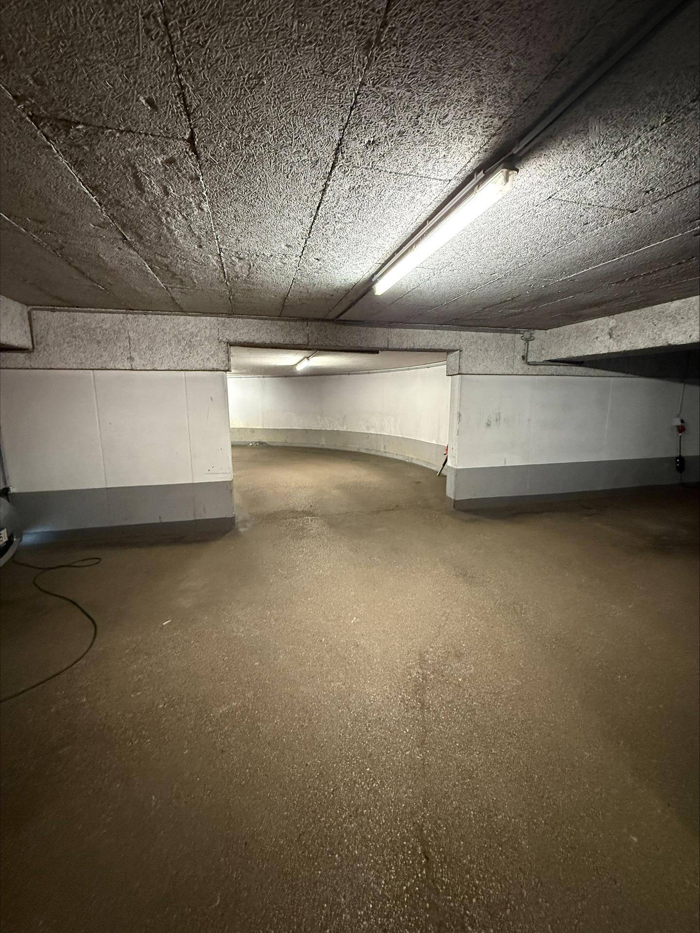 Geräumige Tiefgarage mit Betonboden und Deckenbeleuchtung, bietet ausreichend Platz.