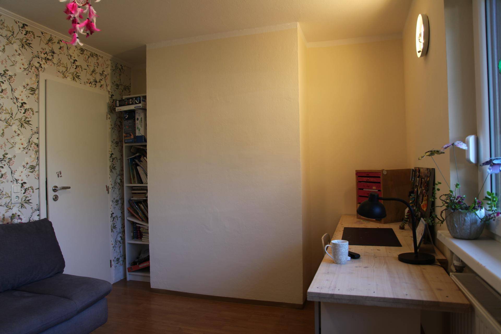 Arbeitszimmer mit Schreibtisch, Bücherregal und floraler Tapete.