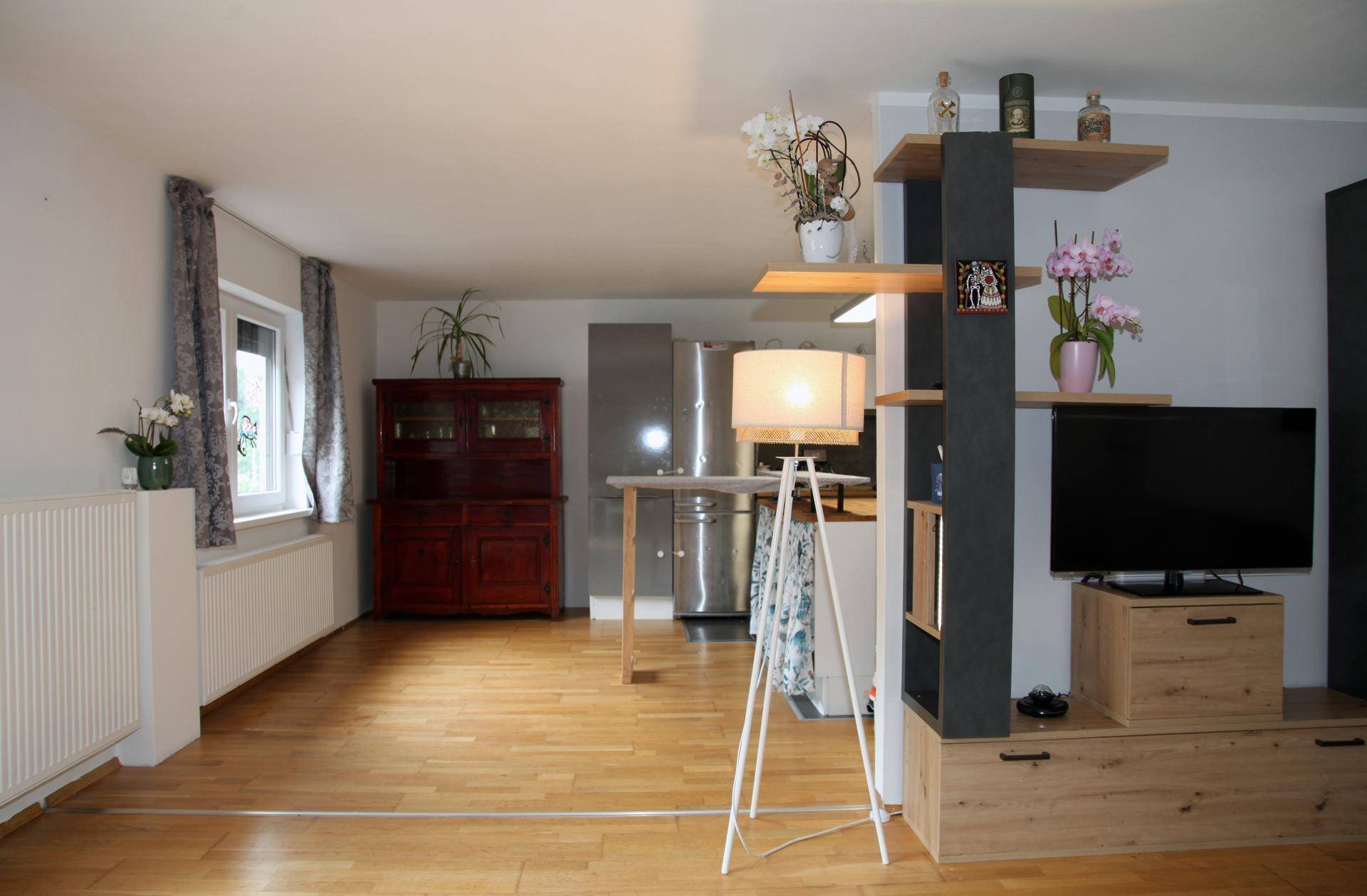 Offener Wohnbereich mit Holzboden, Fenster und Blick in die Küche.
