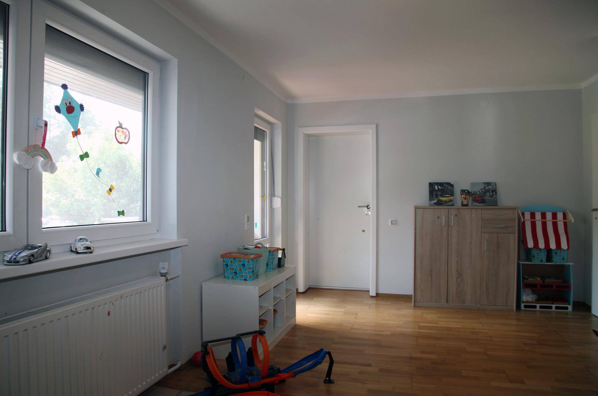 Helles Kinderzimmer mit Holzboden und großen Fenstern.