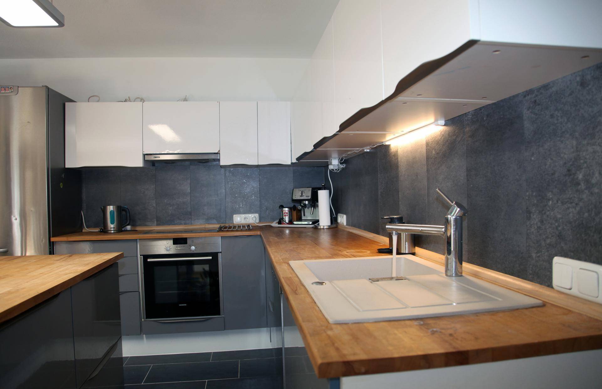 Moderne Küche mit grauen und weißen Schränken, Holz-Arbeitsplatten und integrierten Geräten.