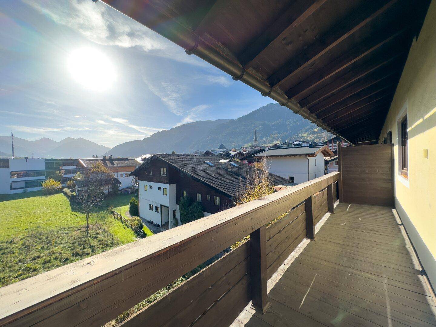 Sonniger Balkon mit Holzboden und Geländer, bietet einen weiten Blick auf die umliegende Berglandschaft.