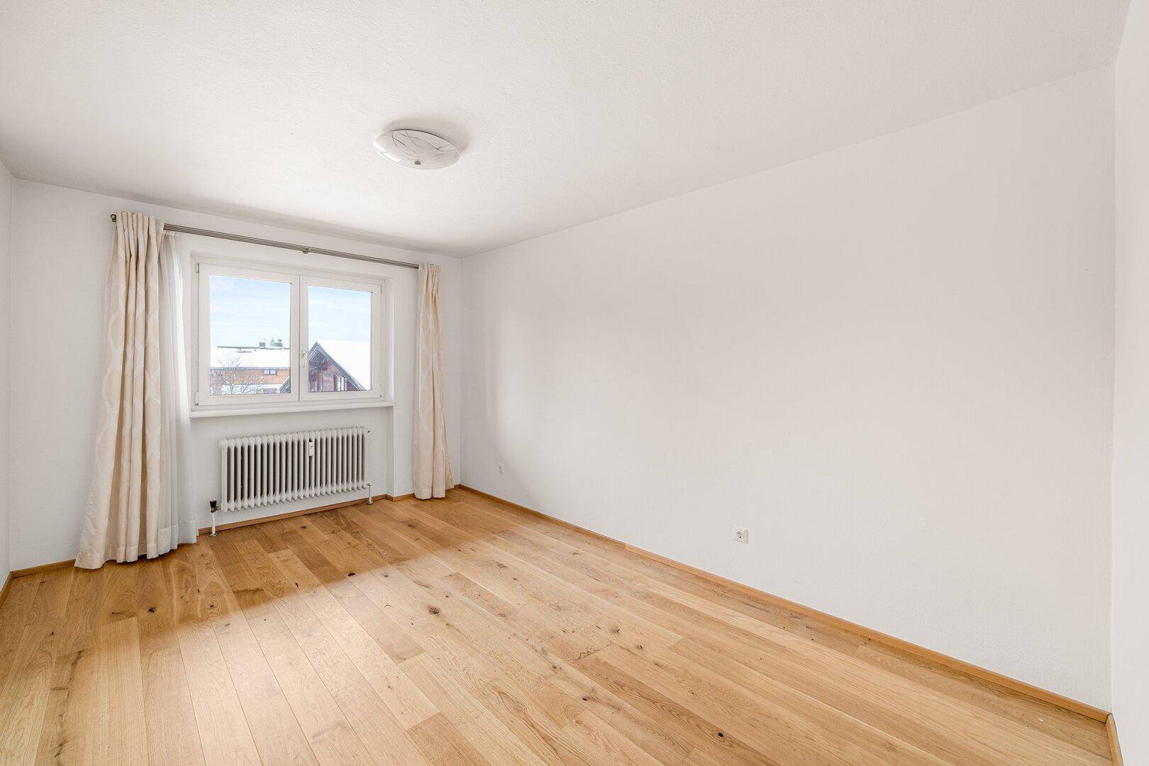 Helles Schlafzimmer mit Eichenparkettboden und großem Fenster, das viel Tageslicht hereinlässt.