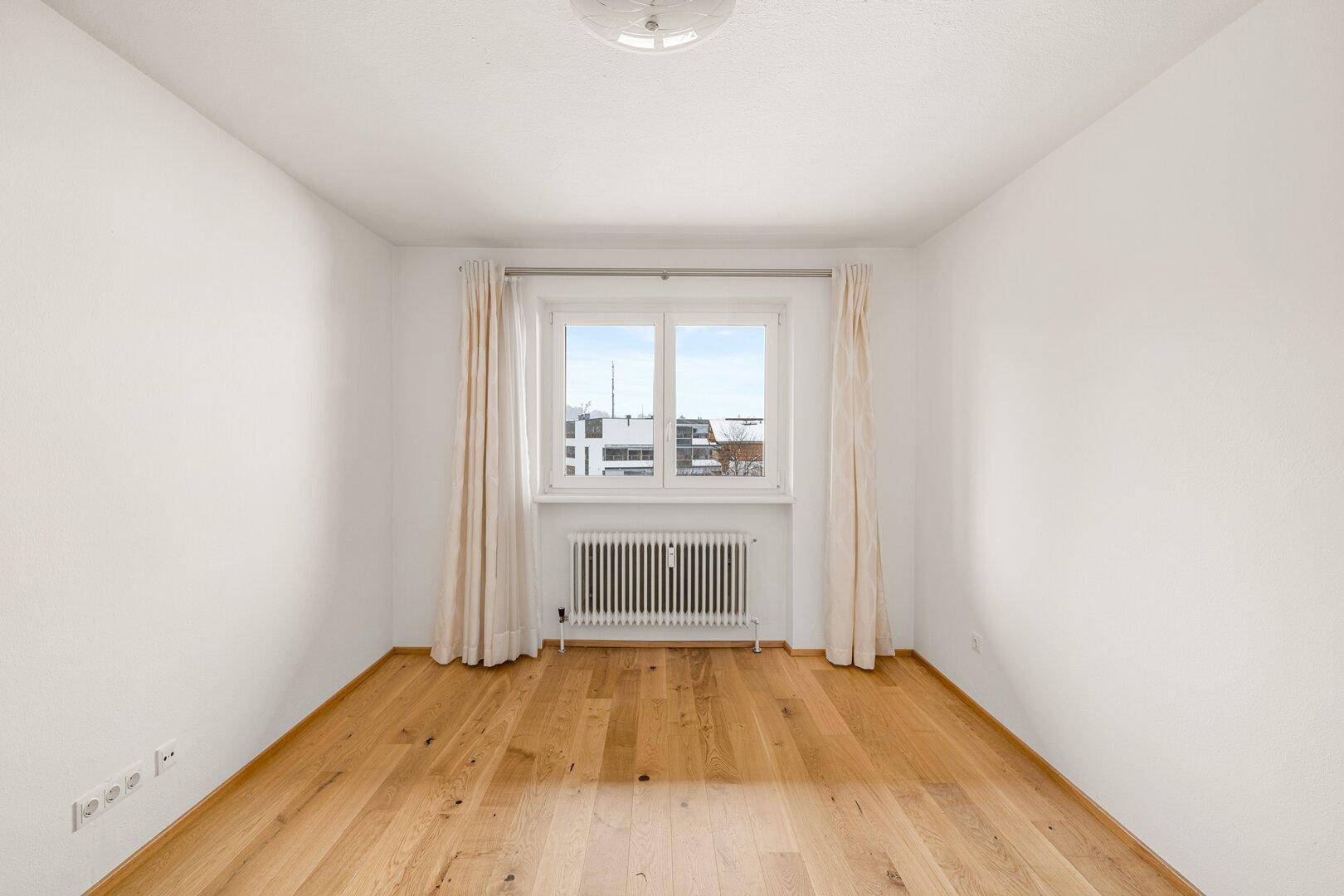 Freundliches Zimmer mit hellem Holzparkett und einem großen Fenster, ideal als Schlaf- oder Kinderzimmer.