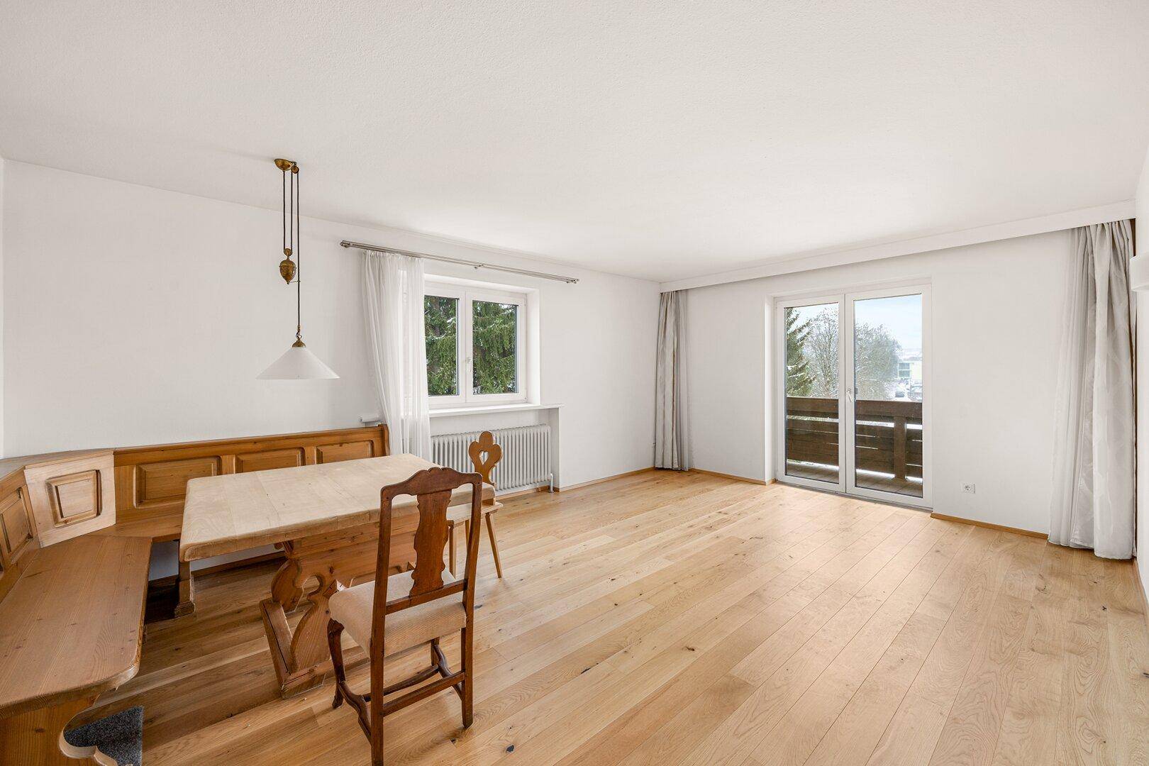Heller Wohn- und Essbereich mit hellem Holzparkett und Zugang zu einem kleinen Balkon.