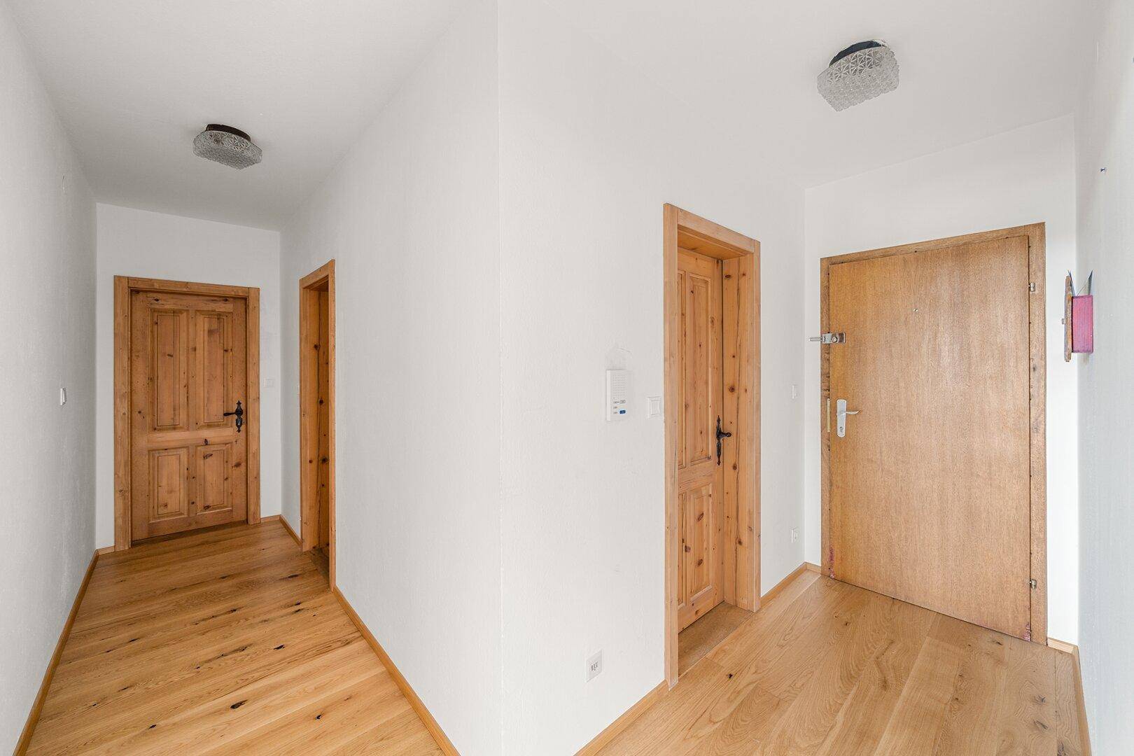 Heller Flur mit Holzparkett und traditionellen Holztüren, der zu den verschiedenen Räumen führt.