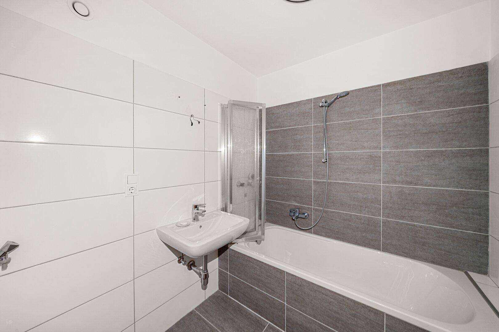 Modernes Badezimmer mit Badewanne, Duschvorrichtung und grauen sowie weißen Fliesen.