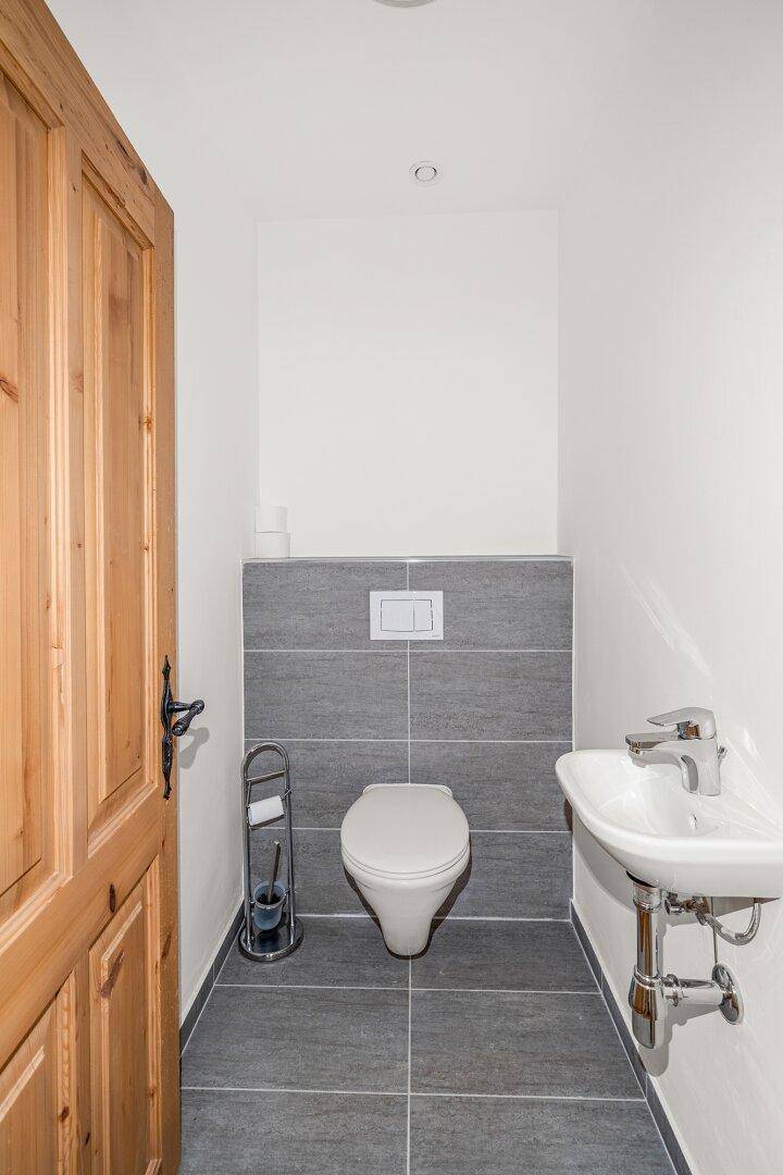 Separates Gäste-WC mit Wand-WC, kleinem Waschbecken und modernen grauen Fliesen.