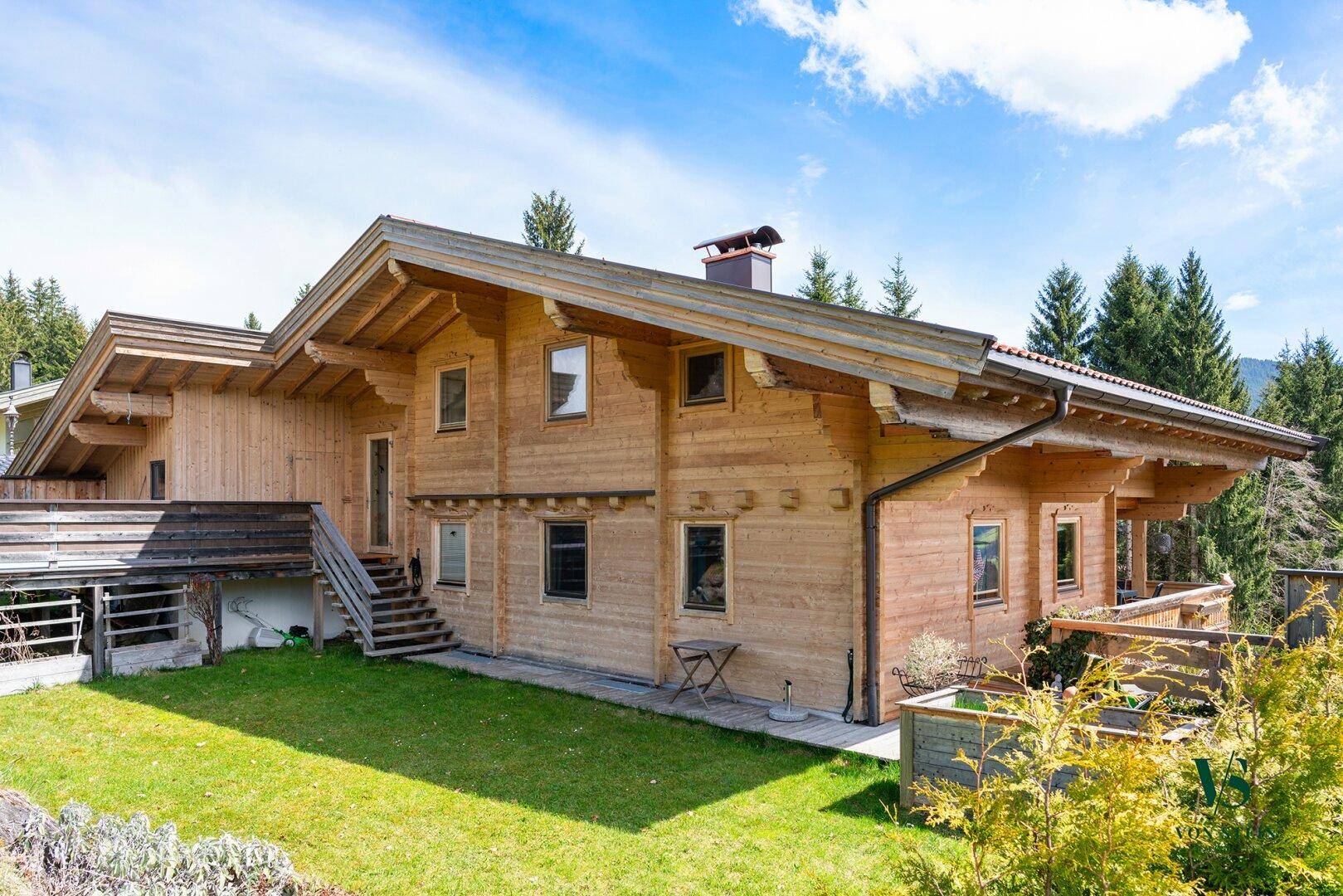 Traditionelles Holzhaus im alpinen Stil mit gepflegtem Rasen und umgebender Natur unter blauem Himmel.