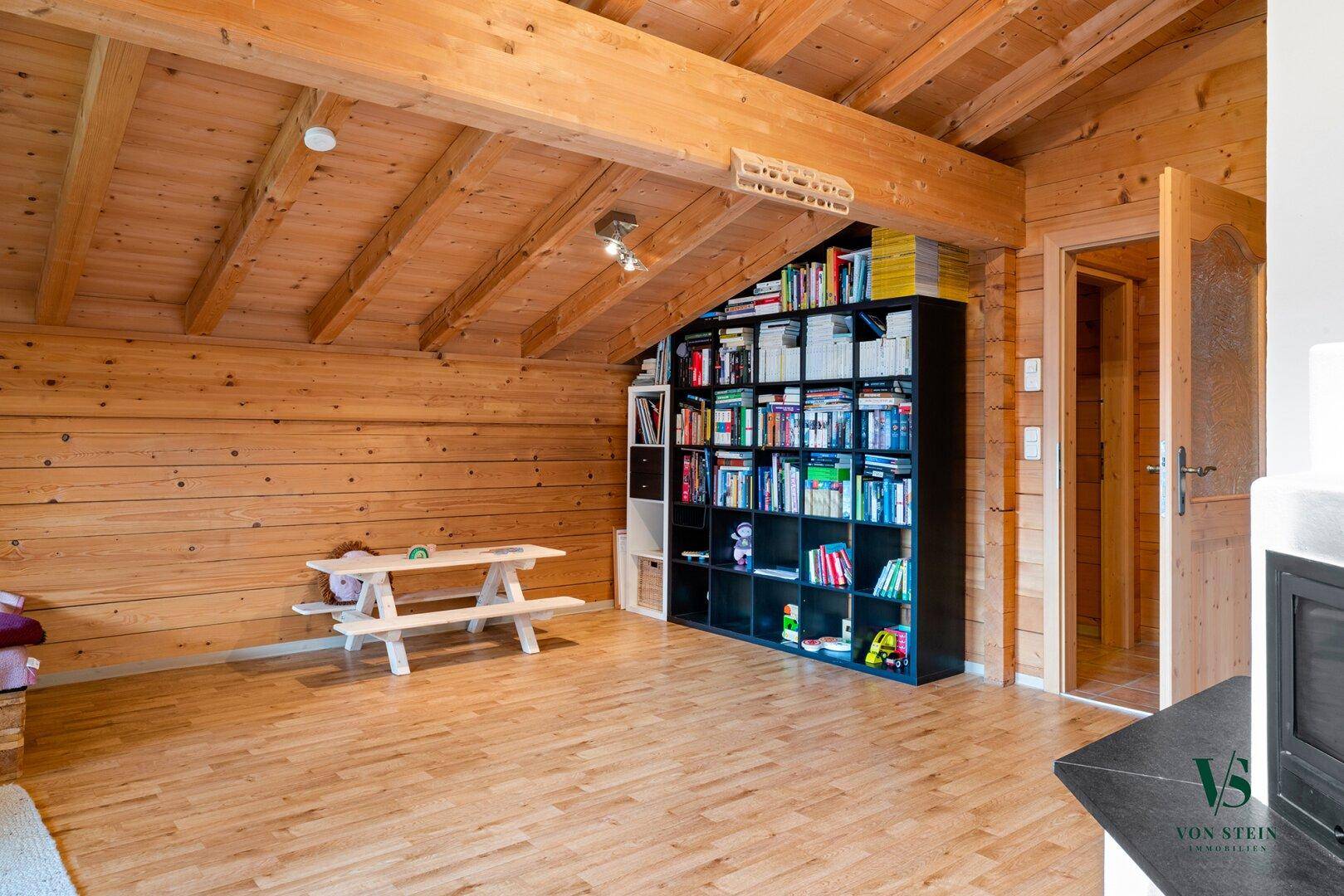 Gemütlicher Wohnbereich im Dachgeschoss mit Holzbalken, Holzverkleidung und einem praktischen Bücherregal.
