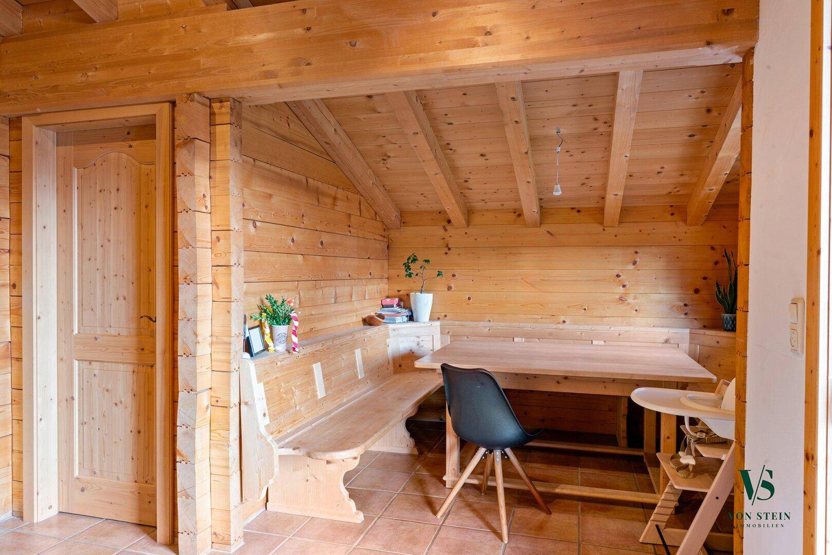 Rustikaler Essbereich mit Holzbänken, Holztisch und traditioneller Holzverkleidung an Wänden und Decke.