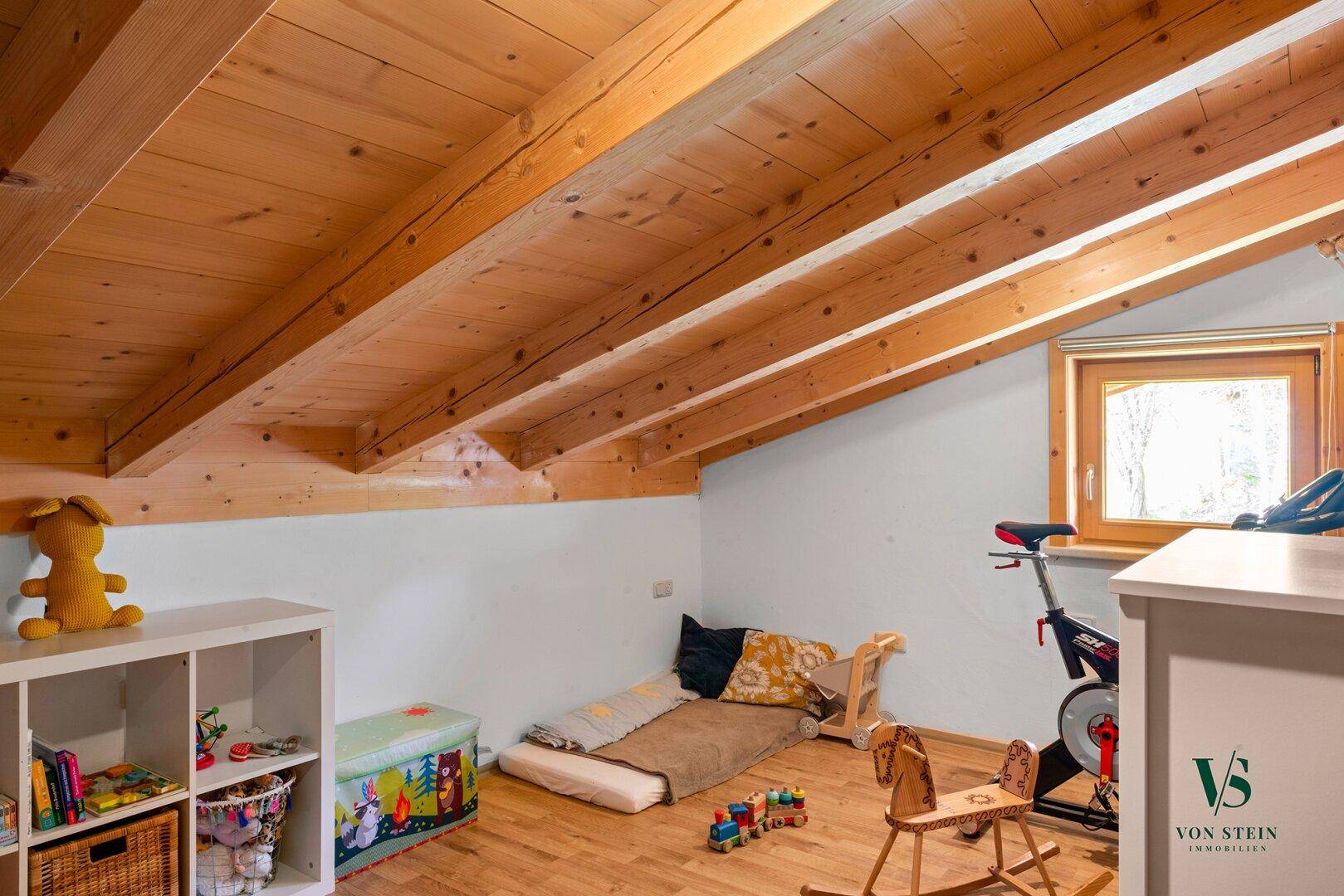 Kinderzimmer im Dachgeschoss mit Holzbalken, Spielzeug und schrägen Wänden für eine gemütliche Atmosphäre.