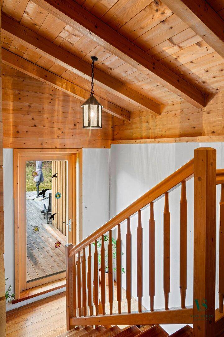 Holztreppe und Flur mit Holzbalkendecke, die zu einem Ausgang ins Freie führt.