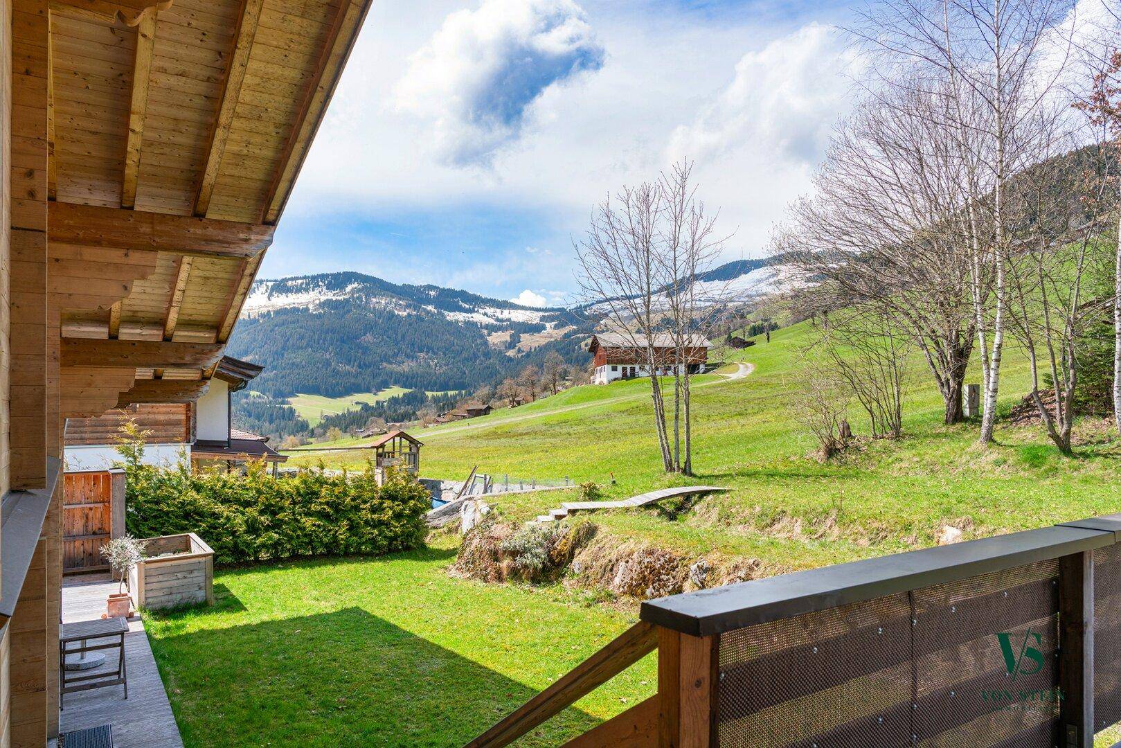 Gepflegter Gartenbereich mit Rasen, Hecken und weitem Blick auf die grüne Berglandschaft.