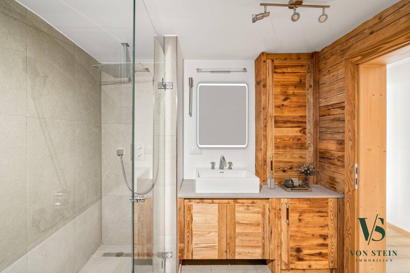Stilvolles Badezimmer mit Holzmöbeln, begehbarer Dusche und modernem Waschbecken.