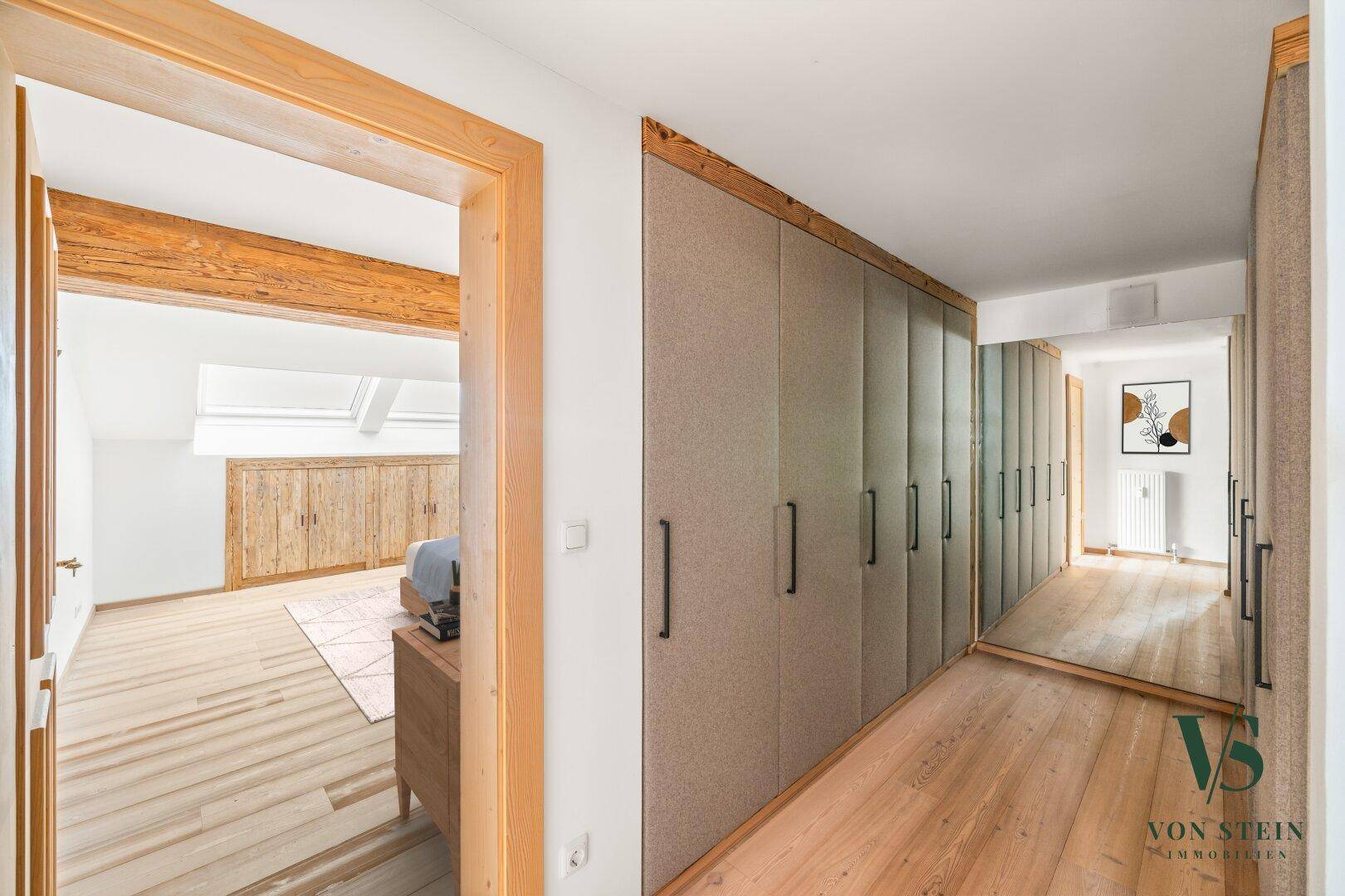 Flur mit Einbauschränken und Zugang zu einem hellen Schlafzimmer im Dachgeschoss.