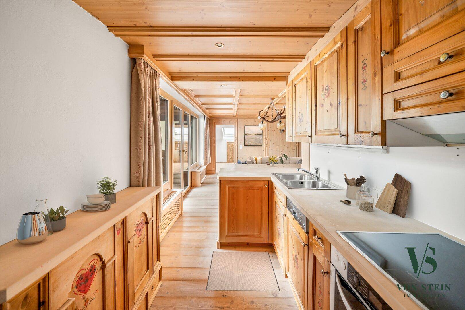 Traditionelle Holzküche mit Einbaugeräten und Blick in den offenen Wohnbereich.