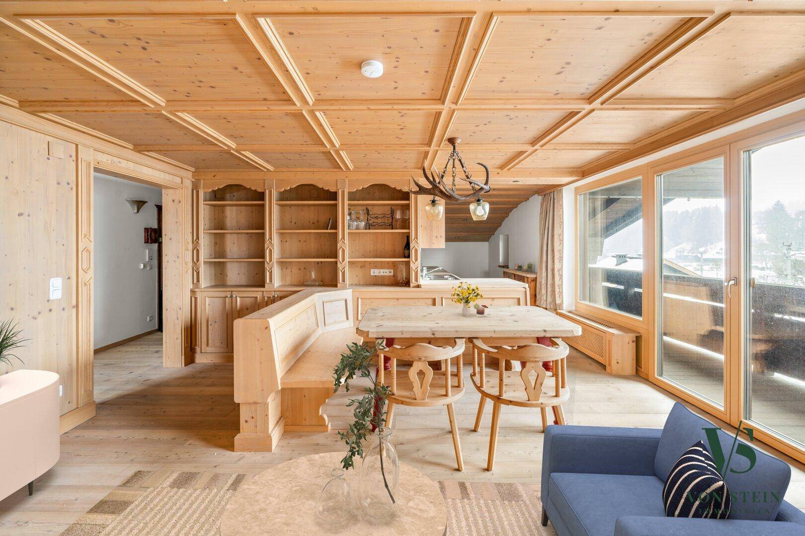 Geräumiger Wohn-Essbereich mit viel Holz, Kassettendecke und Zugang zum Balkon.