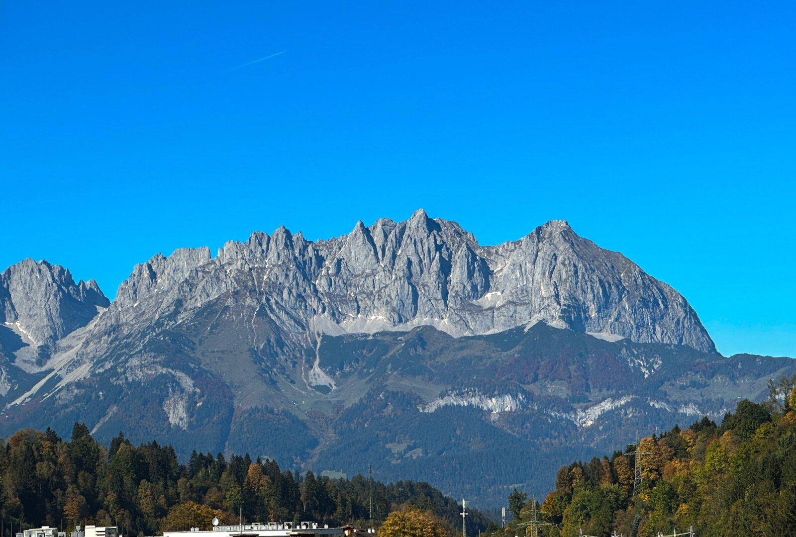 Panoramablick auf die majestätische Bergkette mit bewaldeten Hängen unter blauem Himmel.