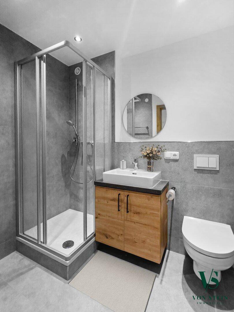 Modernes Badezimmer mit Duschkabine, Einzelwaschbecken und grauen Fliesen.