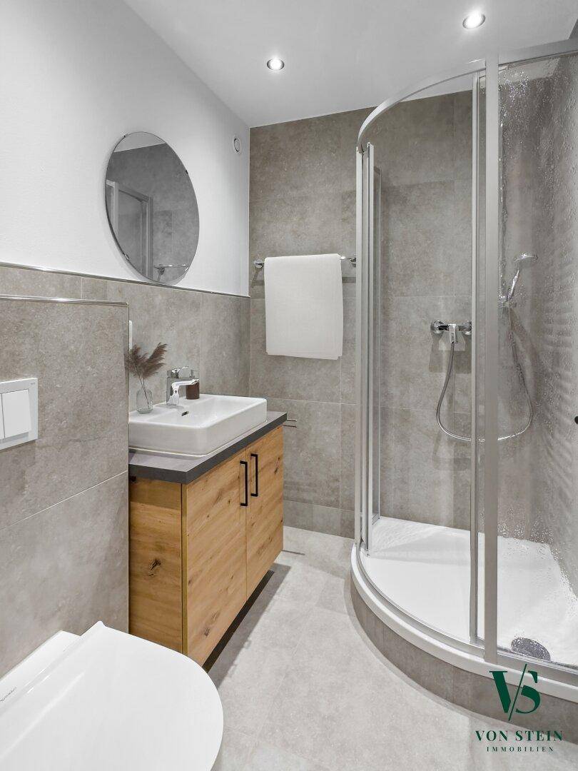 Modernes Badezimmer mit Duschkabine, Einzelwaschbecken und grauen Fliesen.