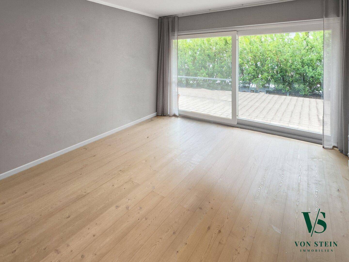 Geräumiger Raum mit Holzboden und großen Fenstern, die viel Tageslicht hereinlassen.
