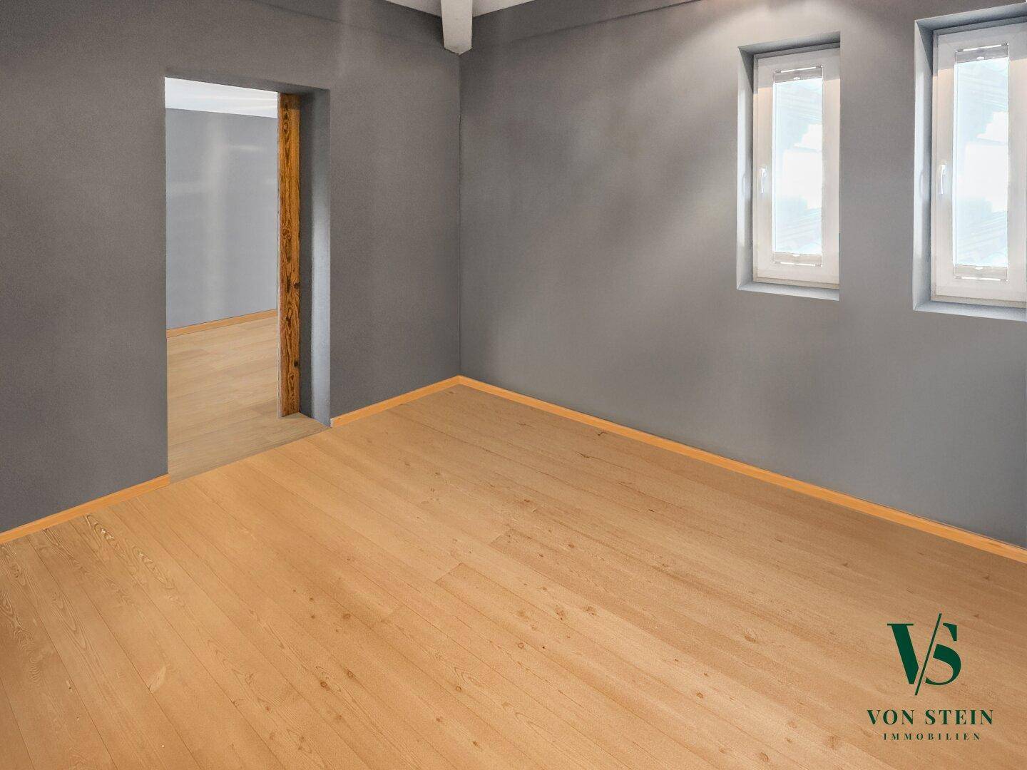 Leerer Raum mit Holzboden und grauen Wänden, bereit zur individuellen Gestaltung.
