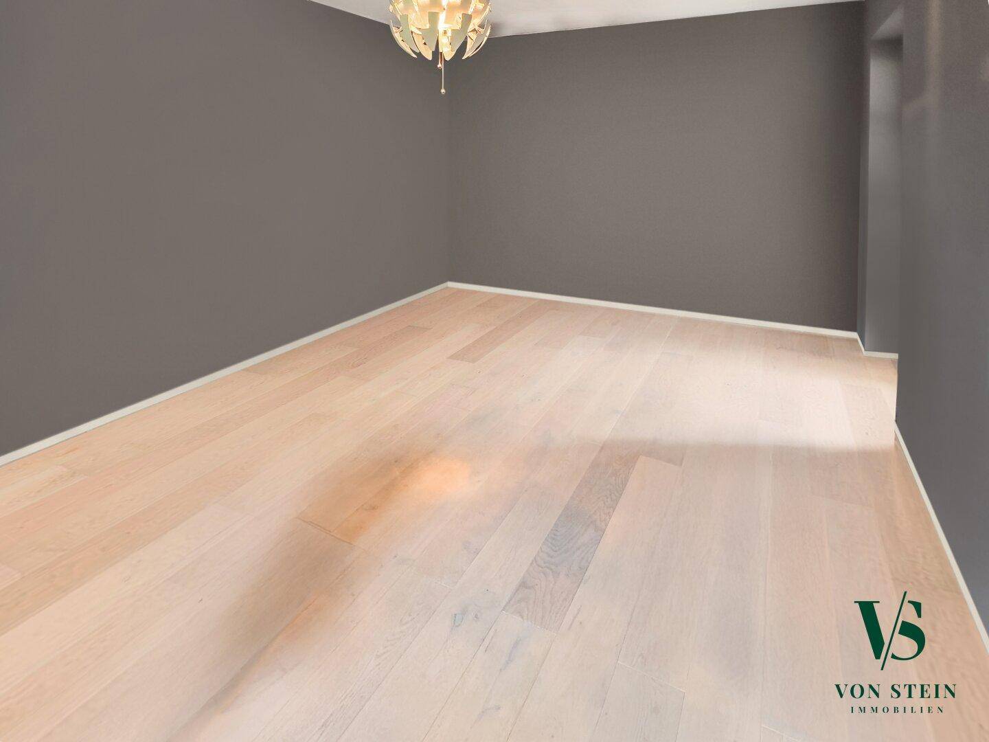 Heller Raum mit Holzboden und grauen Wänden, ausgestattet mit einer Deckenleuchte.