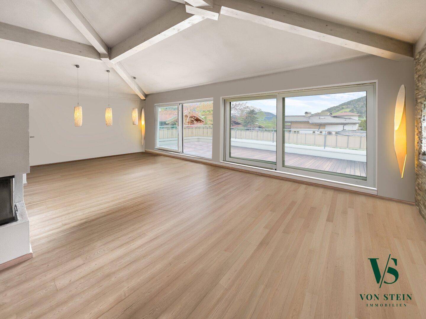 Geräumiges Wohnzimmer mit Holzboden, Kamin und Zugang zu einer großen Terrasse mit Bergblick.