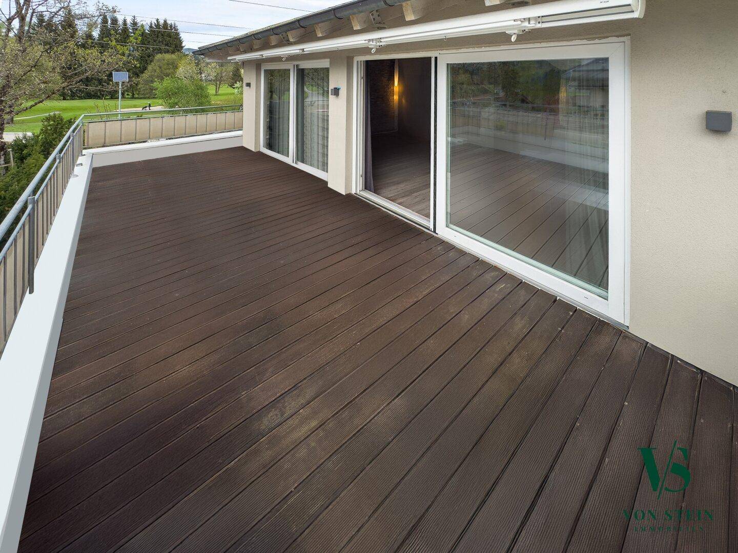 Große Holzterrasse mit Metallgeländer und Zugang zu den Innenräumen durch Schiebetüren.