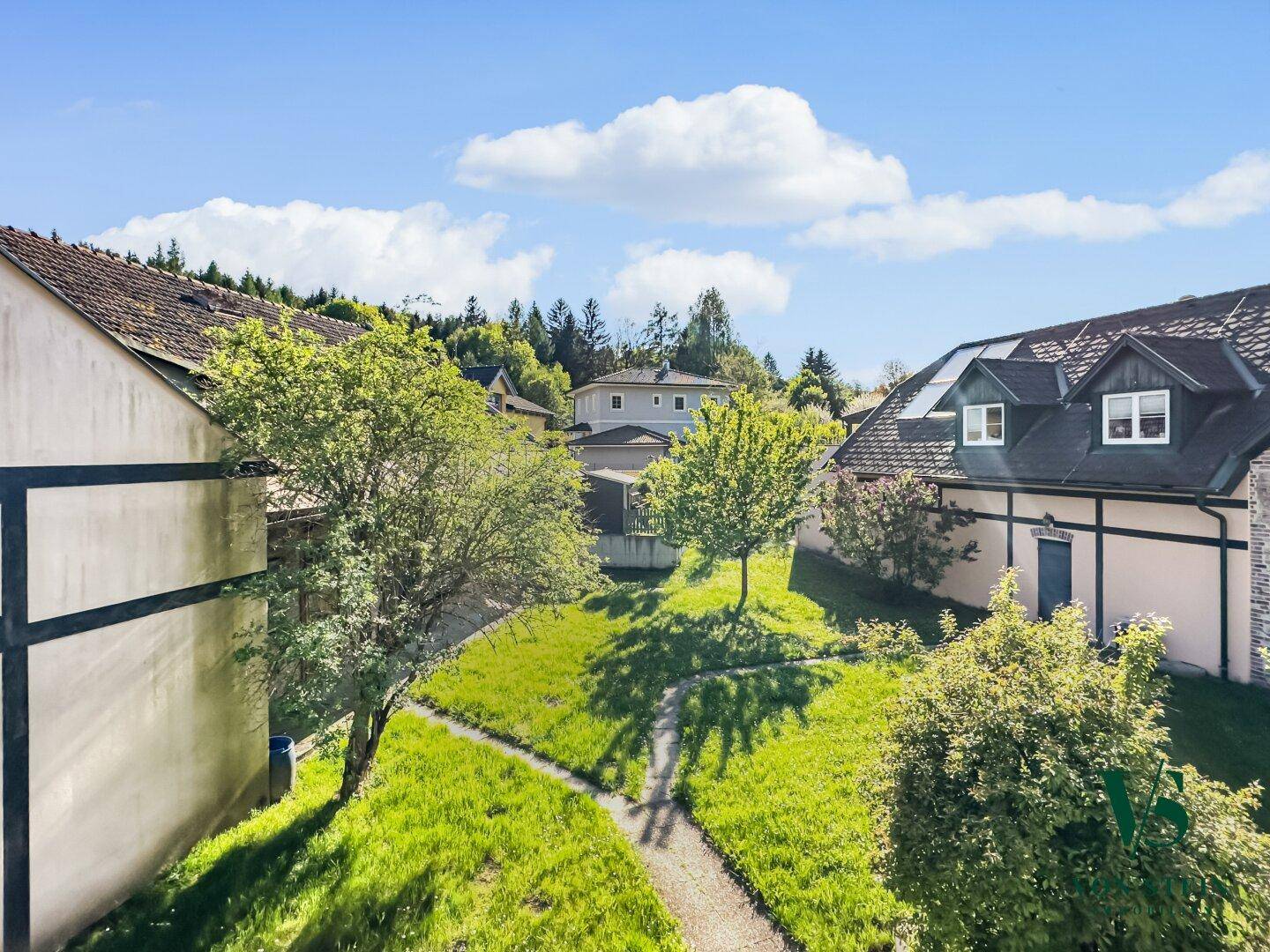 Gepflegter Gartenbereich mit Rasenfläche und Bäumen, umgeben von traditionellen Gebäuden.