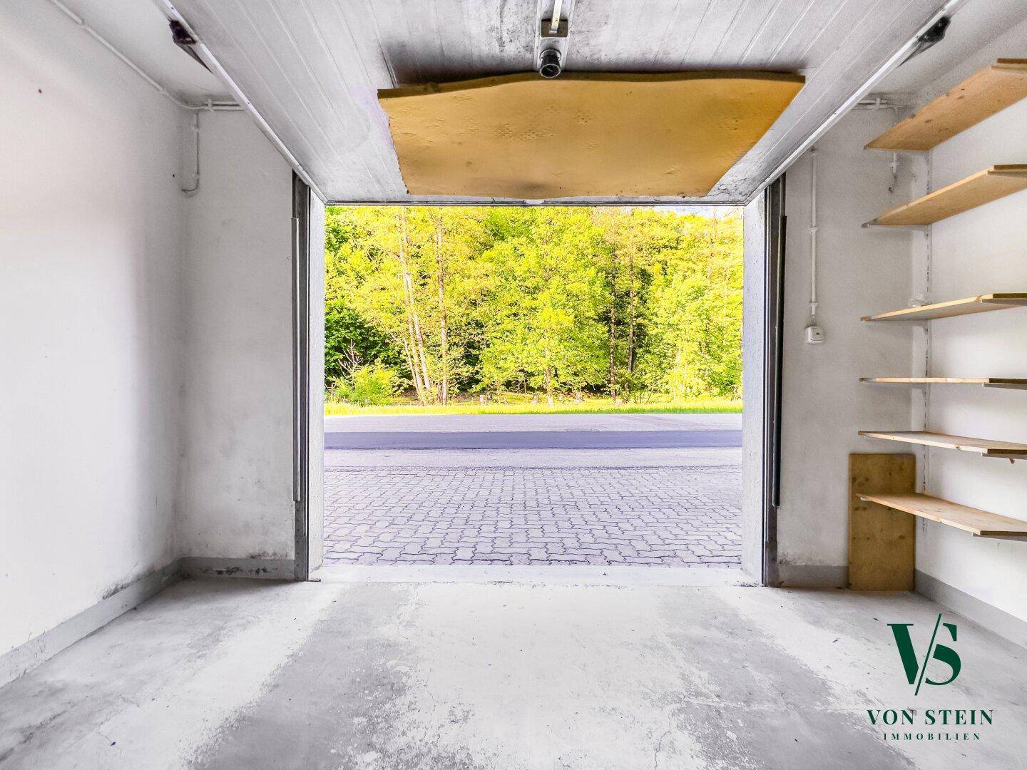 Geräumige Garage mit Betonboden und Blick auf die Straße und Bäume im Freien.