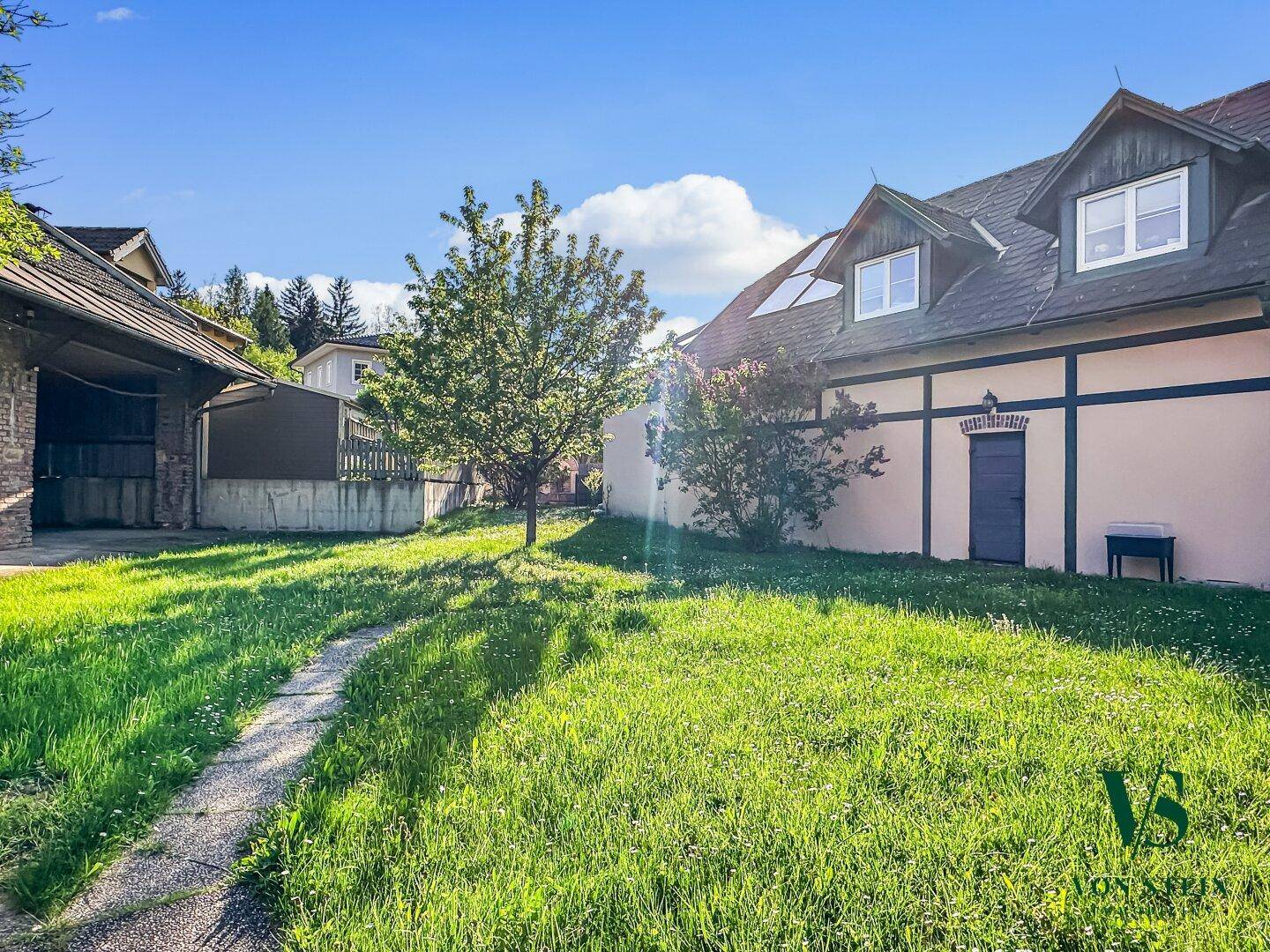 Großer Gartenbereich mit Rasen und Bäumen, umgeben von traditionellen Gebäuden unter blauem Himmel.