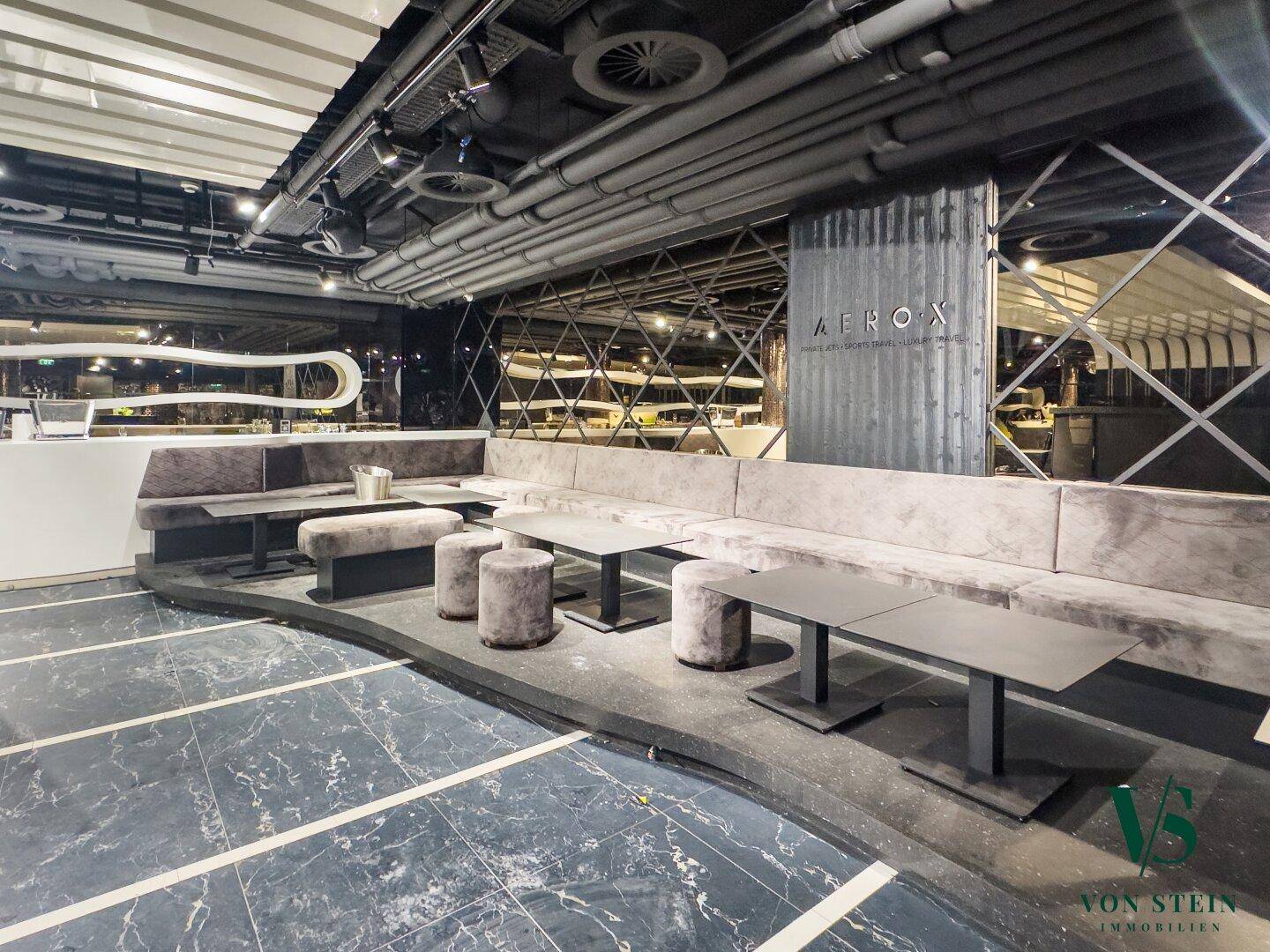Stilvoller Lounge-Bereich mit langen Sitzbänken, dunklem Boden und moderner Deckenkonstruktion.