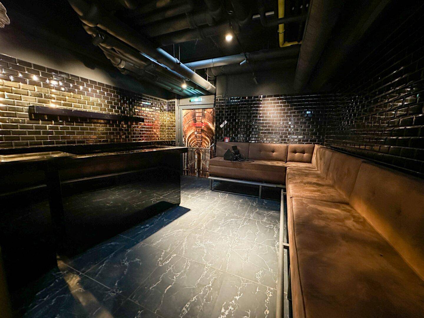 Gemütlicher Lounge-Bereich mit braunen Sitzbänken, dunklen Fliesen und indirekter Beleuchtung.