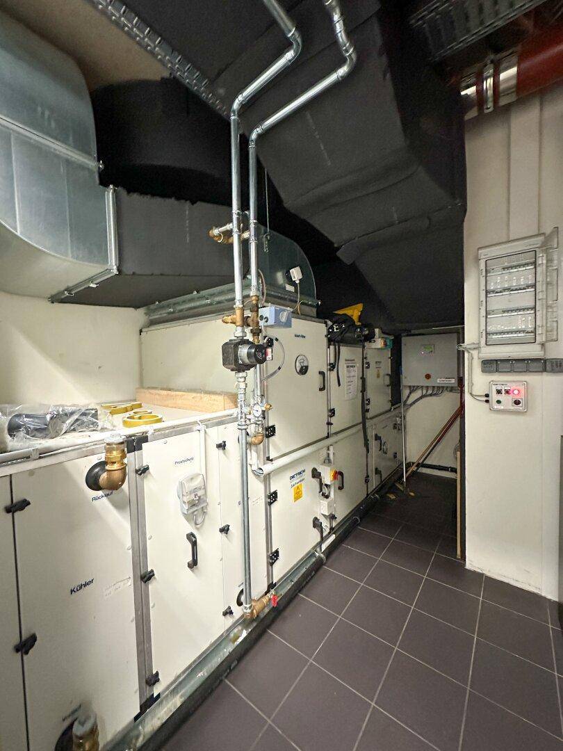 Technischer Raum mit umfangreichen Lüftungsanlagen, Rohren und elektrischen Installationen.