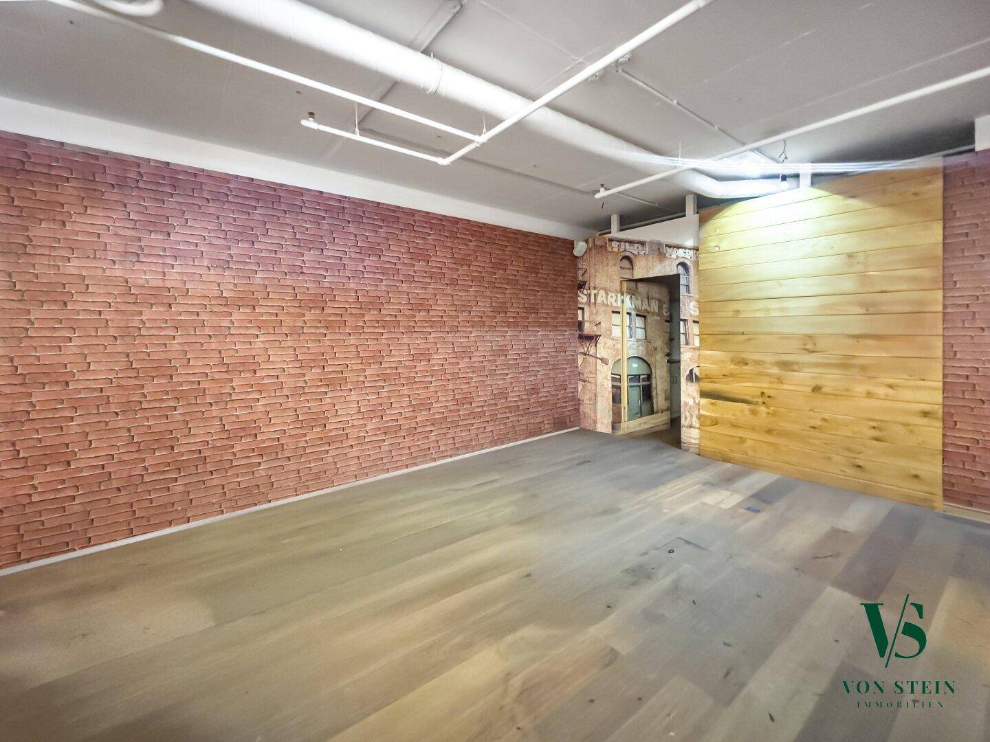Leerer Gewerberaum mit markanter Ziegelwand, Holzakzenten und hellem Bodenbelag, bereit zur Gestaltung.