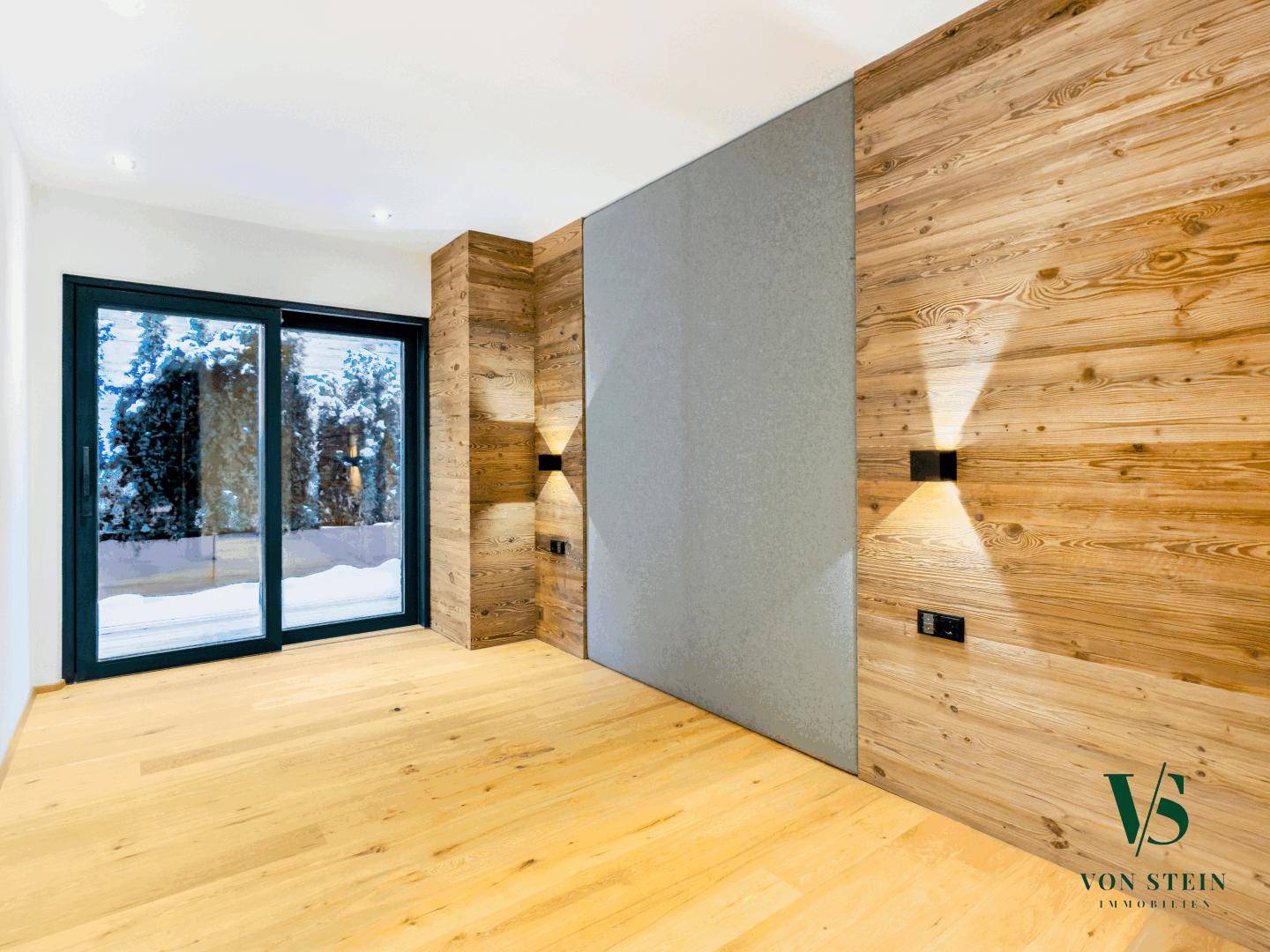 Helles Schlafzimmer mit Holzwänden, Parkettboden und Zugang zu einem Außenbereich.