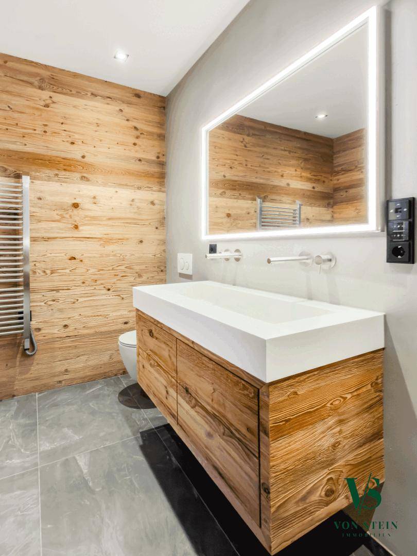Modernes Badezimmer mit Holzvertäfelung, großem Waschtisch und beleuchtetem Spiegel.