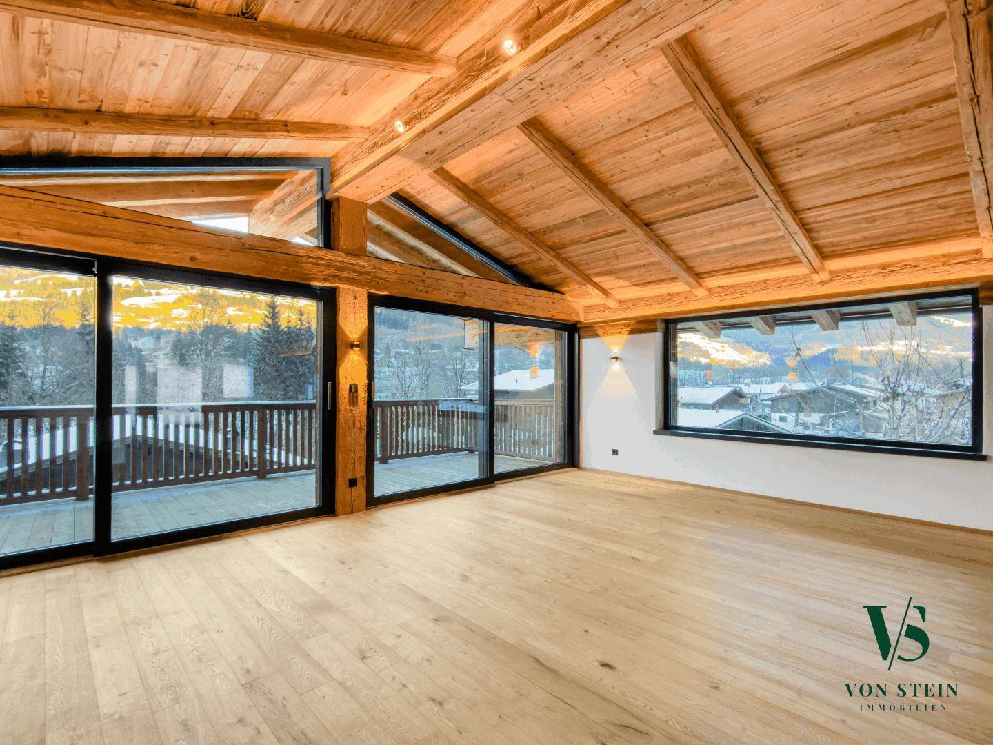 Lichtdurchfluteter Wohnraum mit Holzboden, hohen Decken und weitem Blick auf die verschneite Landschaft.