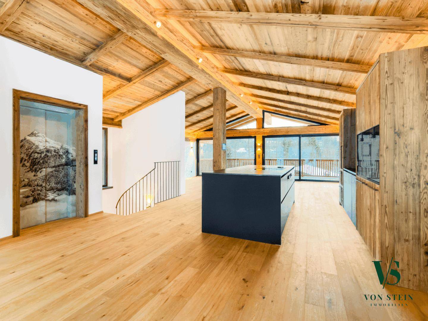 Offener Wohnbereich mit moderner Küche, Holzboden und einem Aufzug mit Bergmotiv.