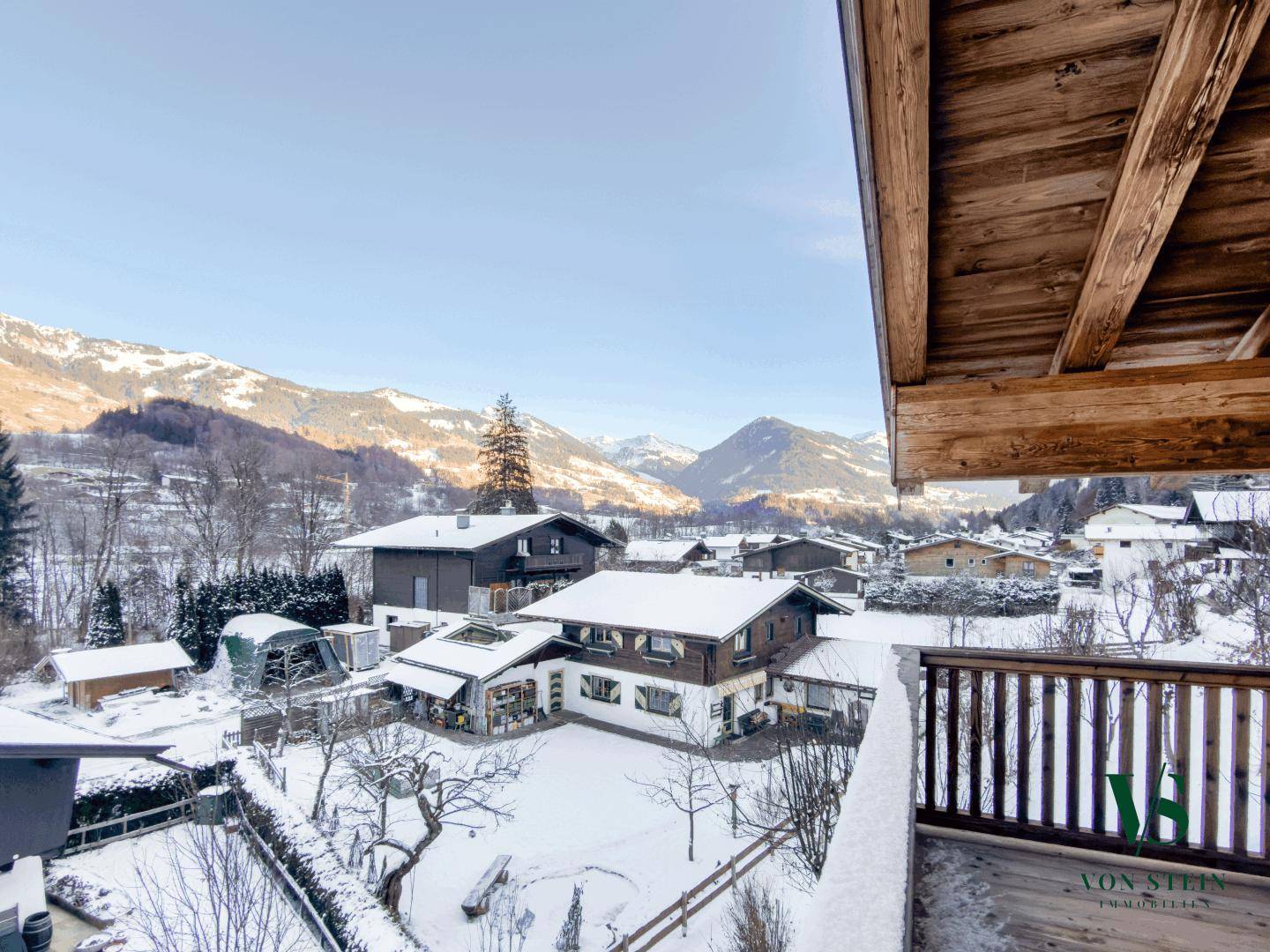 Weitläufiger Blick vom Balkon über die verschneite Dorflandschaft und die majestätischen Berge.