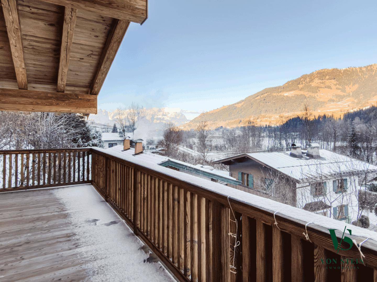 Verschneiter Holzbalkon mit rustikalem Geländer und atemberaubendem Blick auf die umliegenden Berge.
