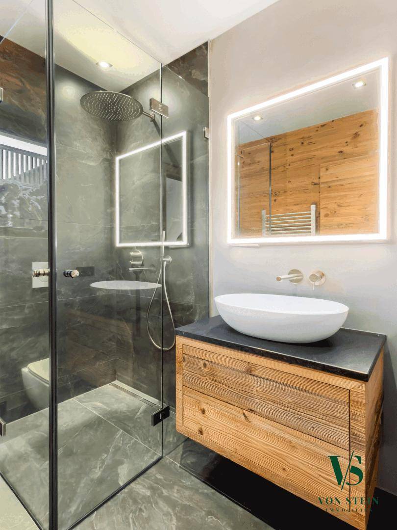 Elegantes Badezimmer mit begehbarer Dusche, Holzwaschtisch und modernem Spiegel.