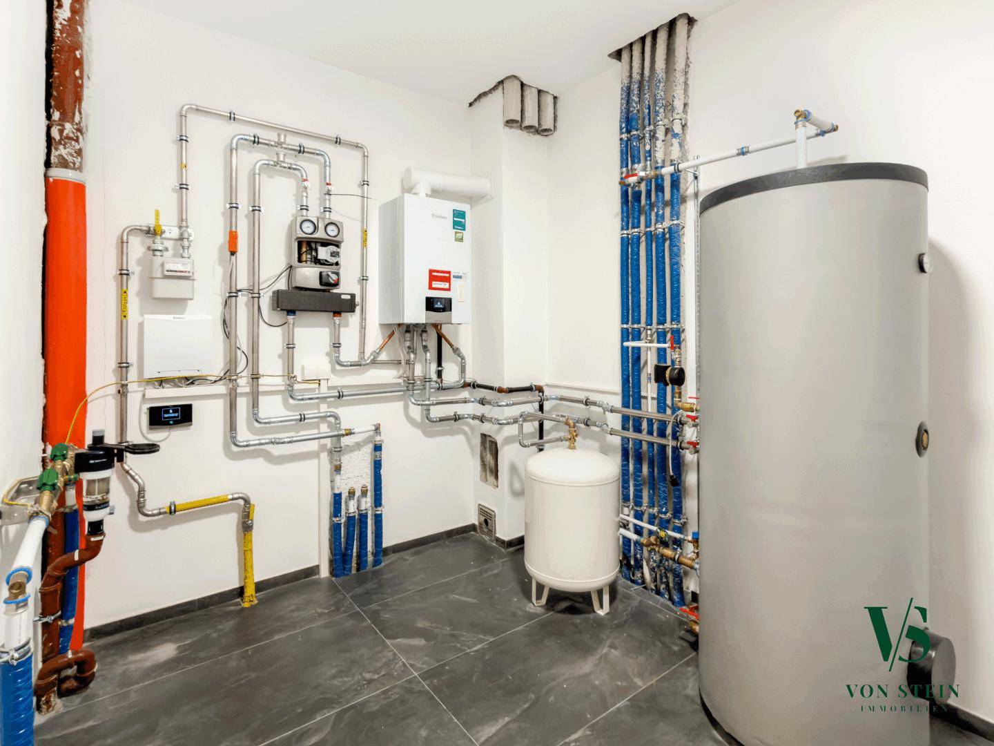 Technischer Raum mit Heizungsanlage, Warmwasserspeicher und umfangreicher Rohrinstallation.